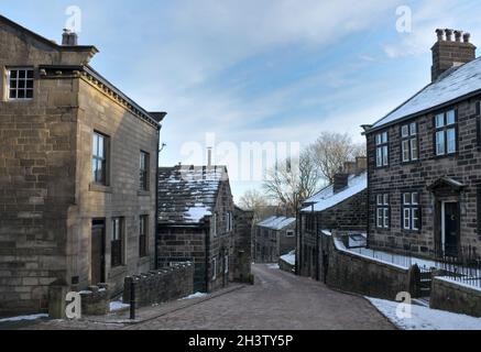 Blick auf die Hauptstraße im Dorf Heptonstall in West Yorkshire mit Schnee auf Dächern mit blauem Winterhimmel Stockfoto