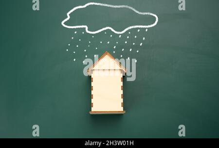 Ein Holzhaus und eine gezeichnete Wolke mit Regen mit weißer Kreide auf einem grünen Kreidetafel. Stockfoto