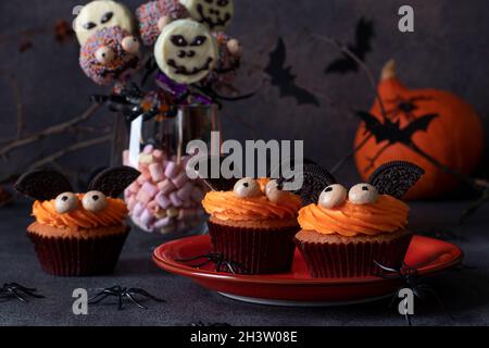 Halloween Treat - Helle süße Kuchen in Form von Fledermäusen, Cake Pops Skelette und Monster mit Schokolade auf dunklem Hintergrund. Verschiedene Süßigkeiten für H Stockfoto