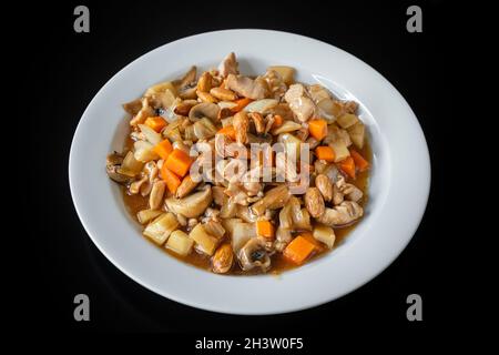 Ein traditionelles chinesisches Gericht aus Hühnereintopf mit Mandeln, Karotten und Pasta. Auf einer Platte auf schwarzem Hintergrund, Nahaufnahme. Stockfoto