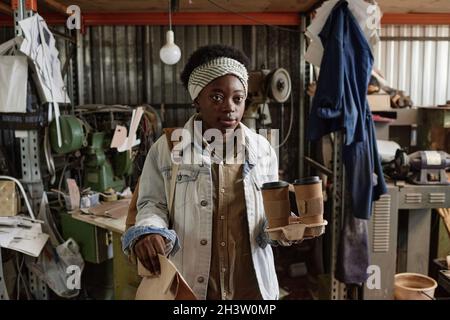 Afrikanisch, die Kaffeetassen und Päckchen mit Frühstück trägt, während sie morgens zur Arbeit kommt Stockfoto