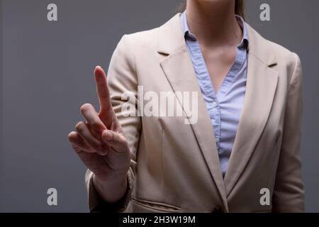 Mittelteil der kaukasischen Geschäftsfrau berührt virtuelle Schnittstelle auf grauem Hintergrund Stockfoto