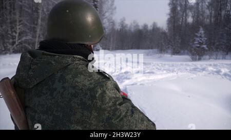 Rückansicht des Soldaten im Winter im Wald. Clip. Der Soldat steht an seinem Posten und bewacht ihn. Militärisches Schutzkonzept. Stockfoto