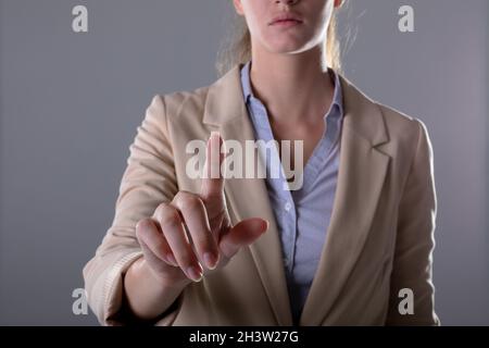 Mittelteil der kaukasischen Geschäftsfrau berührt virtuelle Schnittstelle auf grauem Hintergrund Stockfoto