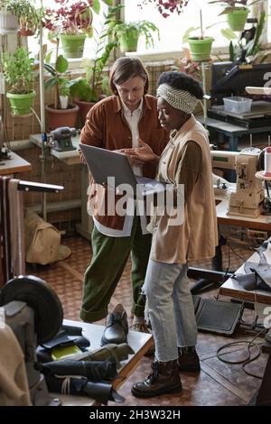 Afrikanischer Designer diskutiert mit einem Geschäftsmann, der einen Laptop benutzt, während er in der Werkstatt steht Stockfoto