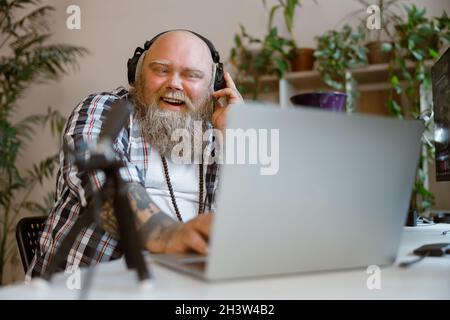 Bärtiger Moderator mit Übergewicht nimmt Audio-Podcast im Heimstudio auf Stockfoto