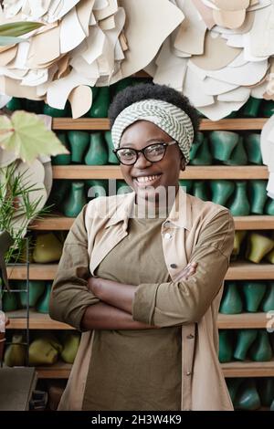 Porträt einer glücklichen afrikanisch lächelnden Frau, die in der Werkstatt mit Schuhen im Hintergrund steht und die Kamera anlächelt Stockfoto