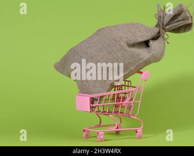 Braune Tasche in einem kleinen Mini-Einkaufswagen auf grünem Hintergrund. Reichtum Stockfoto