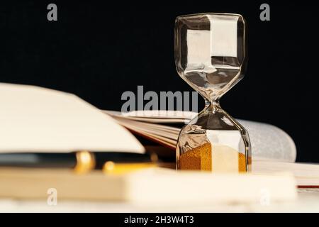 Sandglas auf Holztisch mit geöffnetem Buch aus nächster Nähe Stockfoto