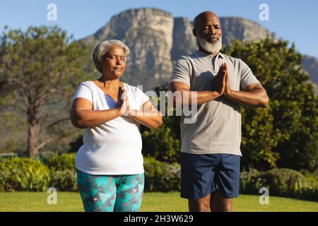 Ein älteres afroamerikanisches Paar meditiert und praktiziert Yoga mit geschlossenen Augen auf dem Land Stockfoto