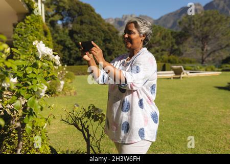 Ältere afroamerikanische Frau, die mit dem Smartphone im sonnigen Garten fotografiert Stockfoto