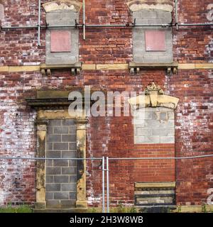 Fassade eines verlassenen, verlassenen alten Hauses mit zerbröckelnden Ziegelwänden und versperrten Fenstern Stockfoto