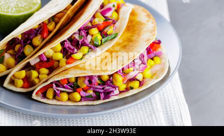 Vegane Tacos mit Mais, purpurem Kohl und Tomaten auf einem grauen Teller. Mexikanische Tacos mit Gemüse und Guacamole auf grauem Hintergrund. Nahaufnahme Stockfoto