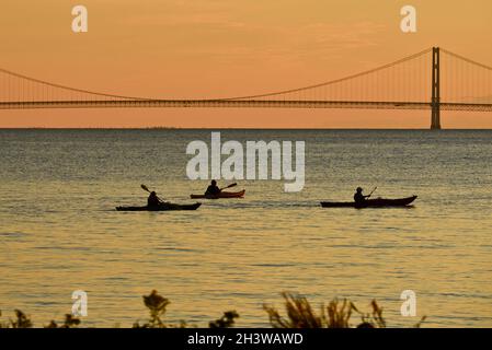 Kajakgruppe während einer geführten Tour auf dem Lake Huron bei einem friedlichen Sonnenuntergang, mit Mackinac Bridge in der Ferne, Mackinac Island, Michigan, USA. Stockfoto