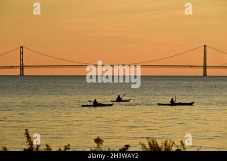 Kajakgruppe während einer geführten Tour auf dem Lake Huron bei einem friedlichen Sonnenuntergang, mit Mackinac Bridge in der Ferne, Mackinac Island, Michigan, USA. Stockfoto