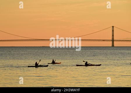 Kajakgruppe während einer geführten Tour auf dem Lake Huron bei einem friedlichen Sonnenuntergang, mit Mackinac Bridge in der Ferne, Mackinac Island, Michigan, USA. Stockfoto