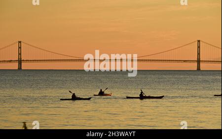 Kajakgruppe während einer geführten Tour auf dem Lake Huron bei einem friedlichen Sonnenuntergang, mit Mackinac Bridge in der Ferne, Mackinac Island, Michigan, USA. Stockfoto