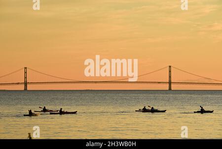 Kajakgruppe während einer geführten Tour auf dem Lake Huron bei einem friedlichen Sonnenuntergang, mit Mackinac Bridge in der Ferne, Mackinac Island, Michigan, USA. Stockfoto