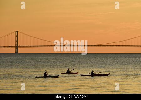 Kajakgruppe während einer geführten Tour auf dem Lake Huron bei einem friedlichen Sonnenuntergang, mit Mackinac Bridge in der Ferne, Mackinac Island, Michigan, USA. Stockfoto