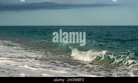 Kleine Welle stürzt an einem Strand in kristallklarem Wasser Stockfoto