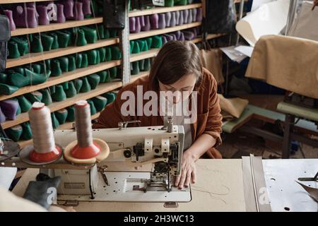 Schuhmacherin, die am Tisch sitzt und die Nähmaschine bei ihrer Arbeit benutzt, näht neue Schuhe Stockfoto