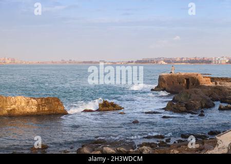 Alexandria, Ägypten - 13. Dezember 2018: An einem stürmisch sonnigen Tag befindet sich der Fischer an den Küstenfelsen des Montazah-Strandes Stockfoto