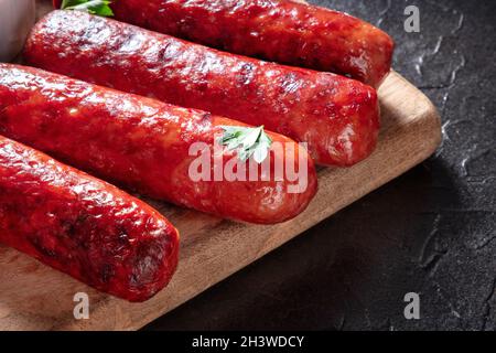 Köstliche Grillwürste auf einem rustikalen Holzbrett auf schwarzem Hintergrund Stockfoto