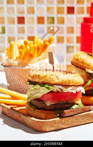 Köstliche hausgemachte Burger auf Holztablett in hellem Sonnenlicht. Burger mit Kalbsschnitzel, Pamidor, Käse, roten Zwiebeln, Salat, aru Stockfoto