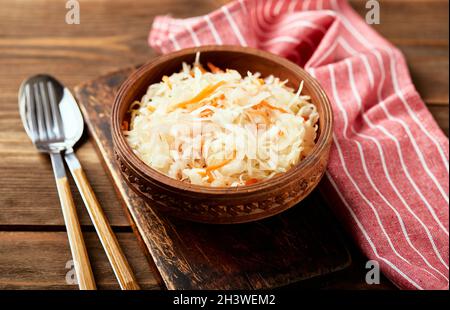 Sauerkraut, fermentierter Kohl mit Karotten in Schüssel auf Holzboden mit Kopierraum. Stockfoto