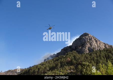 Der Wildfire-Hubschrauber geht, um Wasser auf ein Feuer am Hang eines steilen, felsigen Hügels zu gießen. Stockfoto