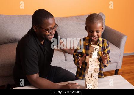 Vorschuljunge zu Hause, glücklich über Block Turm baute er mit Ermutigung von seinem Vater, beide lächelnd Stockfoto