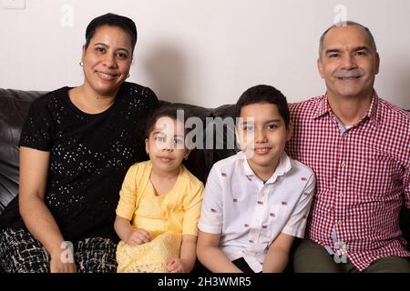 Porträt einer Familie, die auf der Couch sitzt, eines 4-jährigen Mädchens, eines 9-jährigen Bruders, einer Mutter und eines Vaters, die alle die Kamera betrachten Stockfoto