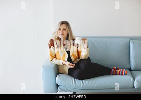 Eine gute Frau, die auf dem Sofa ein heißes Getränk genießt Stockfoto