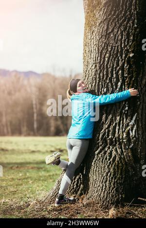 Mädchen in Sportkleidung umarmt einen Baum Stockfoto