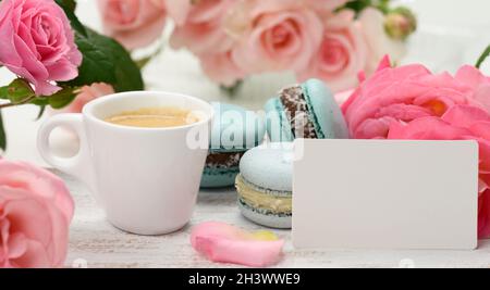 Weiße Visitenkarte und Tasse mit Espresso-Kaffee und weißer Keramikschale mit Kaffee und blauem Macaron auf einem weißen Tisch, Stockfoto