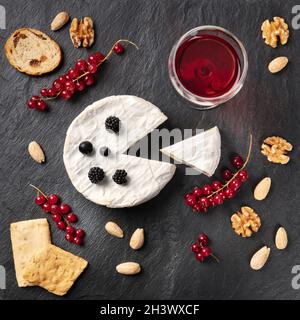 Ein Foto von Camembert mit einem Glas Rotwein, Früchten und Nüssen über dem Kopf Stockfoto