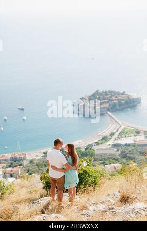 Ein Mann und eine Frau stehen umarmt auf einem Berg Mit Blick auf die Insel Sveti Stefan und Blick auf jeden Andere Stockfoto