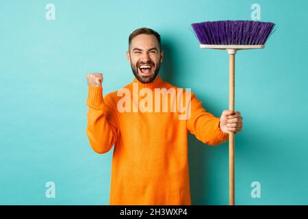 Bild von ermutigten und motivierten Mann immer bereit für die Reinigung, halten Besen und machen Faust Pumpe Geste, über turq stehen Stockfoto