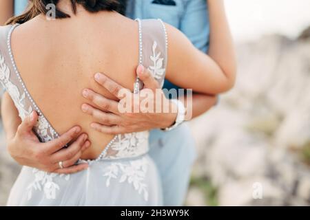 Die Braut und der Bräutigam umarmen die Hände des Bräutigams auf dem Rücken der Braut Stockfoto