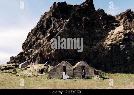 Brautpaar posiert an den alten Häusern, bedeckt mit Moos, auf dem Hintergrund eines felsigen Berges. Hochzeit in Island. Stockfoto