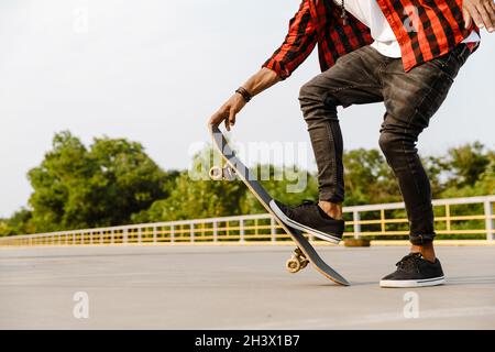 Junger schwarzer Mann trägt karierten kurzen Skateboarding auf dem Parkplatz im Freien Stockfoto