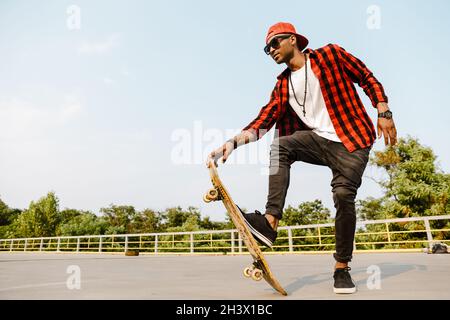 Junger schwarzer Mann trägt karierten kurzen Skateboarding auf dem Parkplatz im Freien Stockfoto