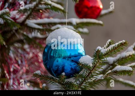 Weihnachtskugeln hängen an einem Baum, der in der Stadt in der Nähe eines Mehrfamilienhauses wächst. Stockfoto