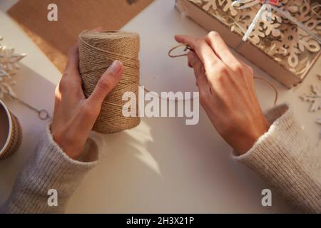 Weibliche Hände wickeln Weihnachtsgeschenke zu Hause. Gemütliches Zuhause. Handgemachte Geschenke. Weihnachtsvorbereitungen. Hochwertige Fotos Stockfoto