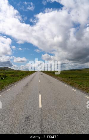 Eine vertikale Ansicht einer asphaltierten Autobahn, die direkt zum Horizont in einer wilden Tundralandschaft führt Stockfoto