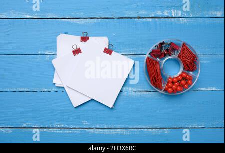 Unbeschriftete quadratische Papierblätter und Schreibwaren mit Büroklammern und Clips auf blauem Holzhintergrund Stockfoto