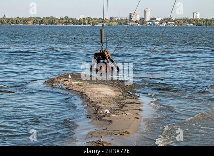 Reinigung der neu entstandenen Insel von Industrieabfällen am Dnjepr River durch einen Bagger. Umweltprobleme moderner Flüsse. Ökologisches Konzept. Stockfoto