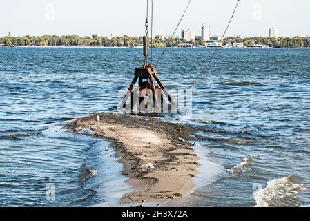 Reinigung der neu entstandenen Insel von Industrieabfällen am Dnjepr River durch einen Bagger. Umweltprobleme moderner Flüsse. Ökologisches Konzept. Stockfoto