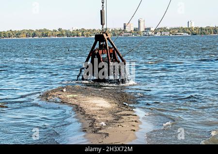 Reinigung der neu entstandenen Insel von Industrieabfällen am Dnjepr River durch einen Bagger. Umweltprobleme moderner Flüsse. Ökologisches Konzept. Stockfoto