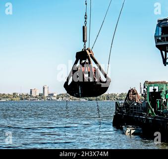 Reinigung der neu entstandenen Insel von Industrieabfällen am Dnjepr River durch einen Bagger. Umweltprobleme moderner Flüsse. Ökologisches Konzept. Stockfoto